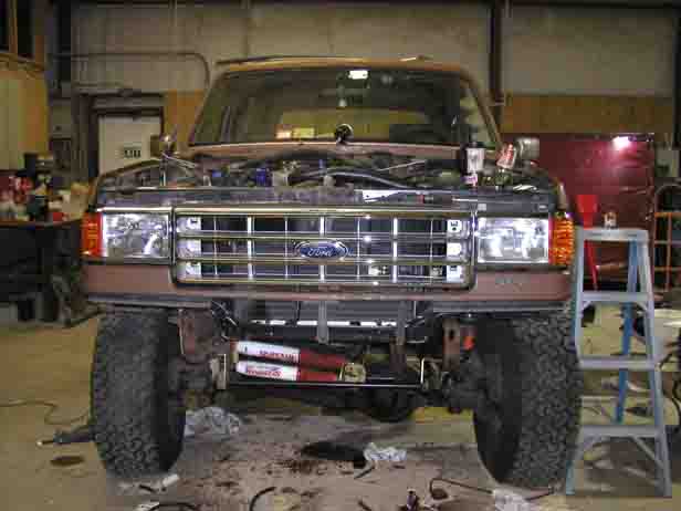 Lifted brown Ford 4x4 front end with bumper and valance removed showing frame and steering stabilizers