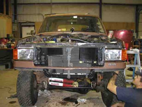 1988 Ford Bronco - Front view of a brown 1988 Ford Bronco undergoing repairs in a garage, with the hood up and the grille removed.