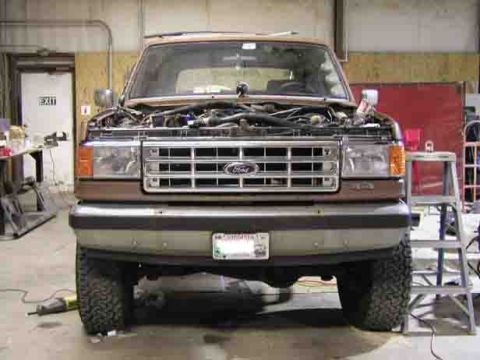 1988 Ford Bronco - Front view of a 1987 Ford Bronco in a garage, hood open to reveal the engine.