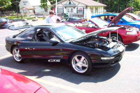 1993 Ford Probe - A black sports coupe with its hood open is parked in a lot with other vehicles.