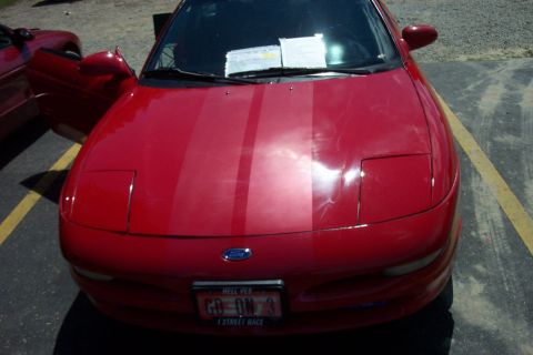 1993 Ford Probe - A red 1993 Ford Probe is parked in a lot, showing its front end and racing stripes. Another vehicle is visible to the left.