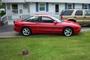 1993 Ford Probe - Side view of a red 1993 Ford Probe parked on grass in front of a building. Another vehicle is visible behind it.