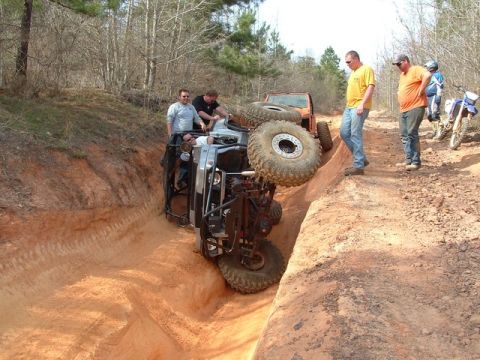 1978 Ford Bronco - An off-road vehicle has overturned in a deep dirt ditch, with onlookers and other vehicles present.