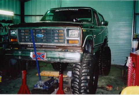 1984 Ford Bronco - This lifted Ford Bronco is on jack stands in a garage, showing its front end and large off-road tires.