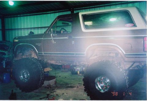 1984 Ford Bronco - This lifted 1984 Ford Bronco features a brown exterior and oversized tires, suggesting off-road modifications.