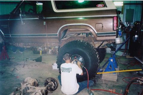 1984 Ford Bronco - Mechanic working on a Ford Bronco in a garage, likely performing maintenance or modification.