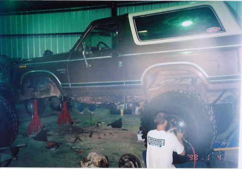 1984 Ford Bronco - A Ford Bronco is elevated on jack stands inside a garage, undergoing mechanical work.