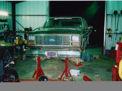 1984 Ford Bronco - A brown 1984 Ford Bronco is shown on jack stands, undergoing work in a garage.