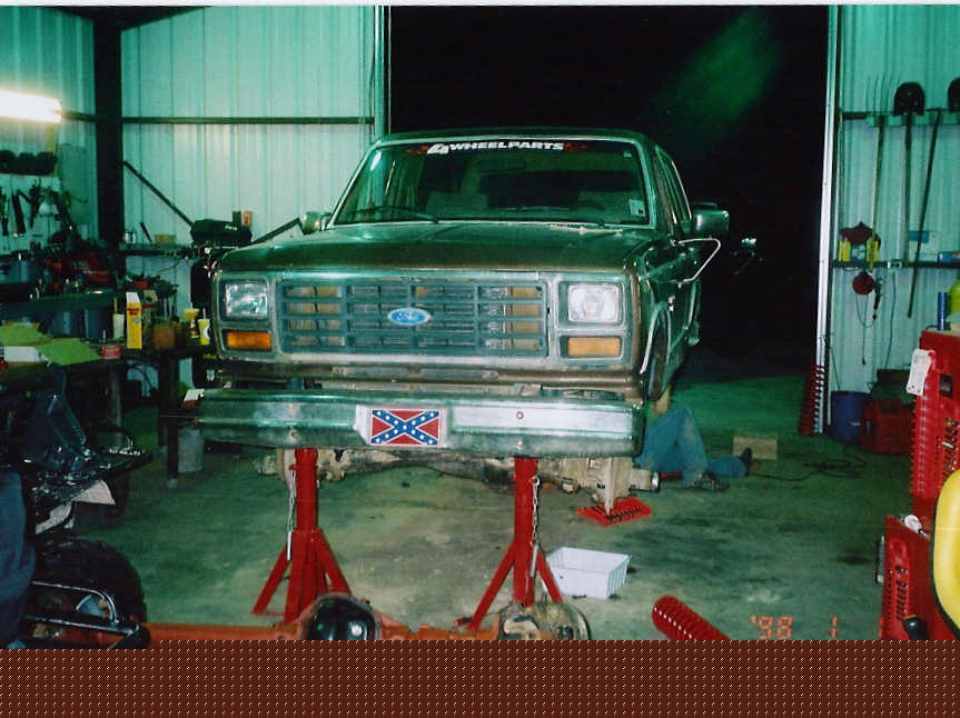 Brown 1984 Ford Bronco front view on jack stands in a garage