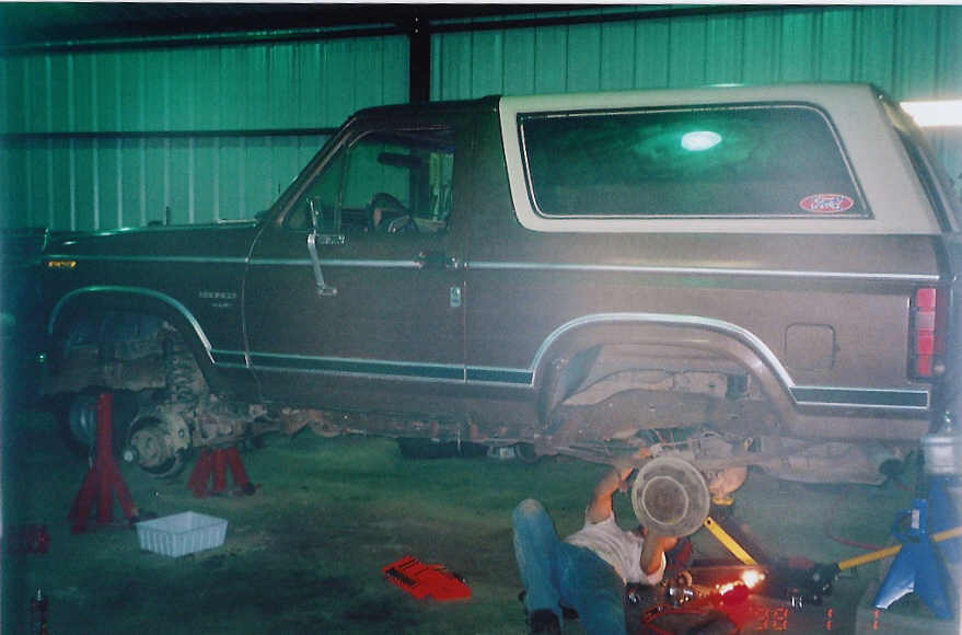 1984 Ford Bronco on jack stands with a person working underneath it