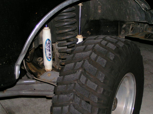 Front suspension closeup showing coil spring, Rancho shock and mud-terrain tire under wheel well
