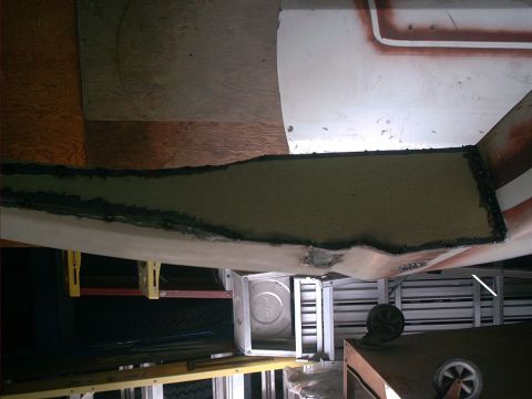1990 Ford Bronco - Sideways-oriented close-up of a cut white body panel edge coated in gray primer or filler with black seam sealer along the flange, showing…