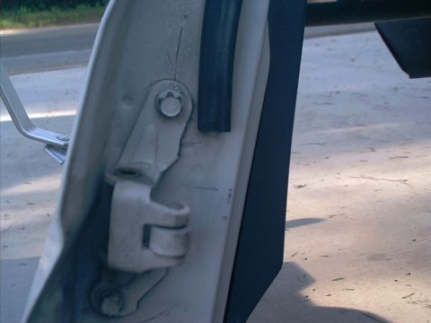 1990 Ford Bronco - Close-up of the white-painted upper door hinge and pin on an open truck door, with the black weatherstrip and door edge trim alongside. The…