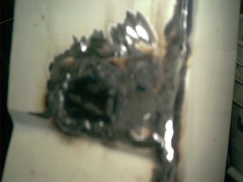 1990 Ford Bronco - Blurry macro shot of a rust repair on a white body panel, where the corroded metal has been ground back to bare shiny steel and built up wi…