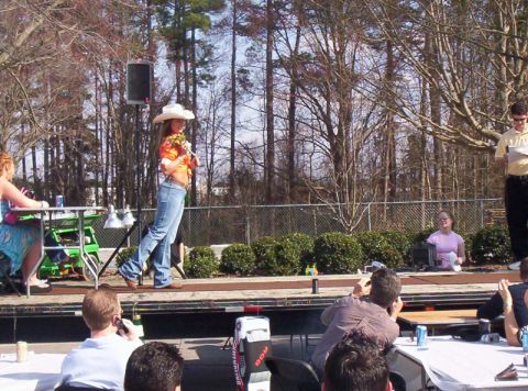 1986 Ford Bronco - An outdoor event is taking place with a woman on stage and an audience watching.
