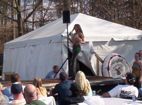 1986 Ford Bronco - A woman stands on a stage in front of a large tent, holding a green item, while an audience watches.