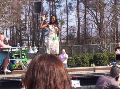 1986 Ford Bronco - A woman waves while holding flowers on an outdoor stage during an event.