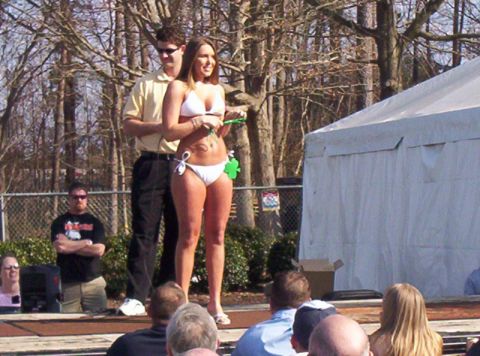 1986 Ford Bronco - Outdoor event with a presenter and a woman in a bikini on a stage, with spectators watching.