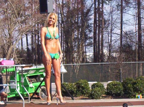 1986 Ford Bronco - A woman poses on a stage during an outdoor event, with a green lift and trees visible behind her.