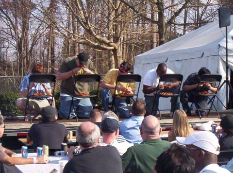 1986 Ford Bronco - Contestants compete in an eating challenge, with spectators watching from the foreground and a large tent set up behind the stage.
