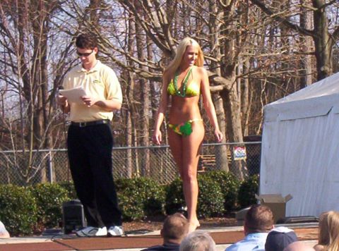 1986 Ford Bronco - A woman in a bikini participates in an outdoor event, with a man holding papers on stage.