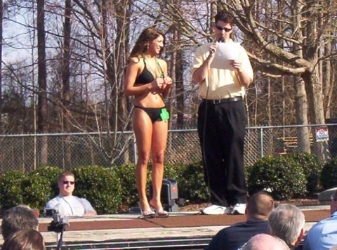 1986 Ford Bronco - A woman in a bikini stands on a stage next to a man speaking into a microphone at an outdoor event.