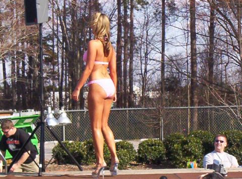 1986 Ford Bronco - A woman in a pink bikini stands on a stage outdoors with trees and a fence behind her.