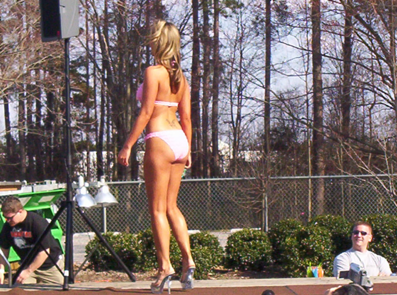 Woman in pink bikini on stage with trees and a fence in the background