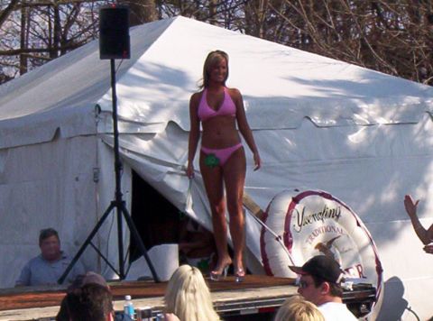 1986 Ford Bronco - A woman stands on a stage during a bikini contest, with a large tent and inflatable ring visible.