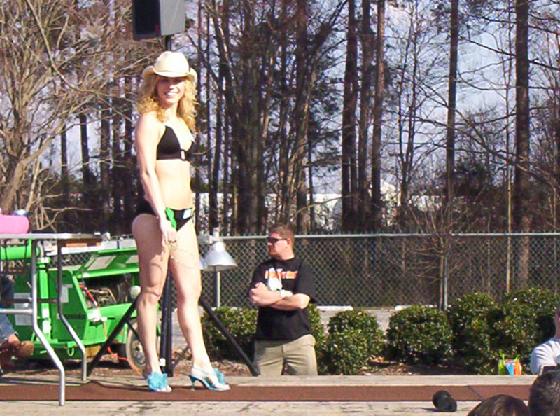Woman in black bikini and cowboy hat on stage with a green generator behind her