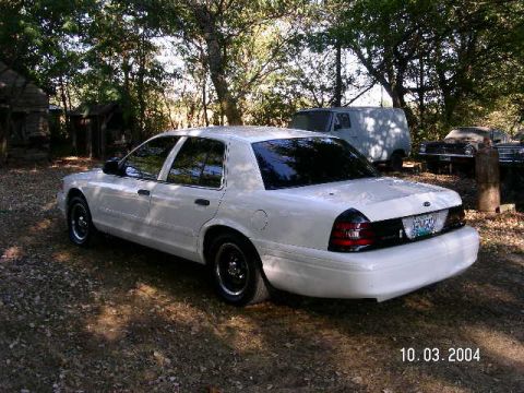 2001 Ford Crown Victoria - White 2001 Ford Crown Victoria parked in a wooded area with other vehicles visible.