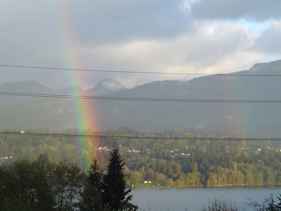 Rainbow over forested mountains and a lake with power lines crossing the foreground