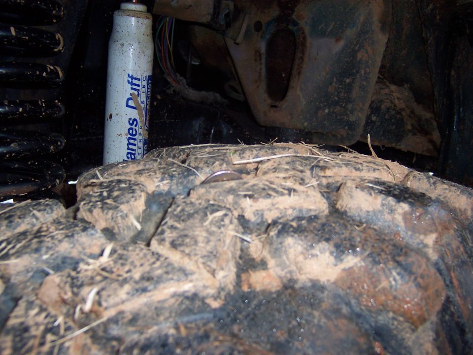 Mud-caked off-road tire and James Duff shock under fender packed with dirt and grass