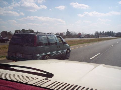 1986 Ford Bronco - A green minivan is seen driving on a highway with other vehicles in the distance.