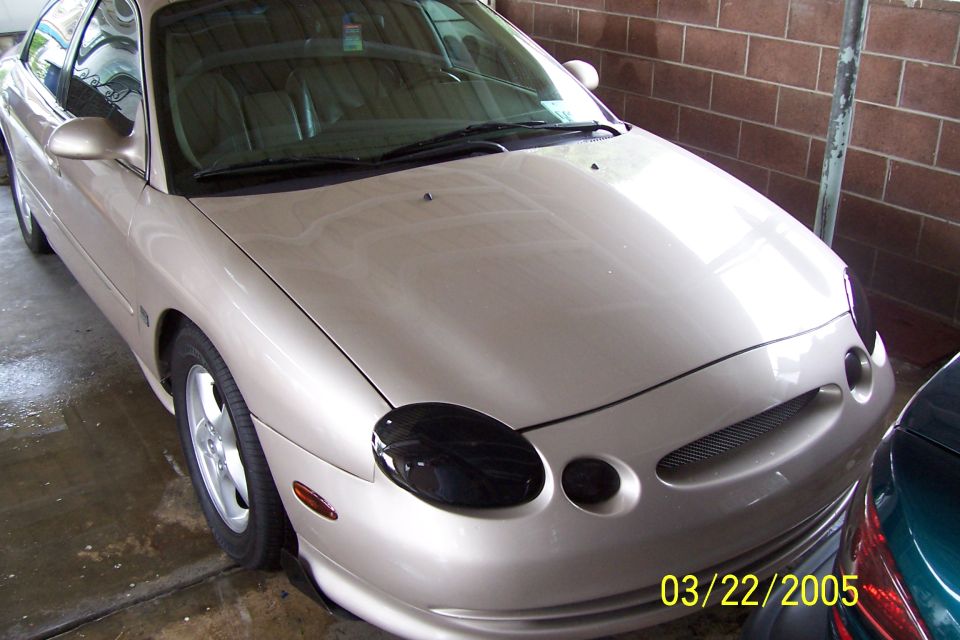 Tan sedan with blacked-out headlights, 3/4 front view
