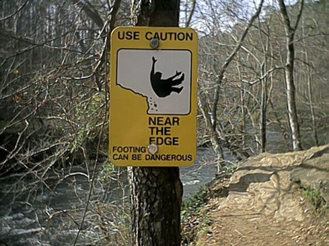 1998 Ford Taurus - A sign warns of danger near the edge of a cliff with a river visible in the background.
