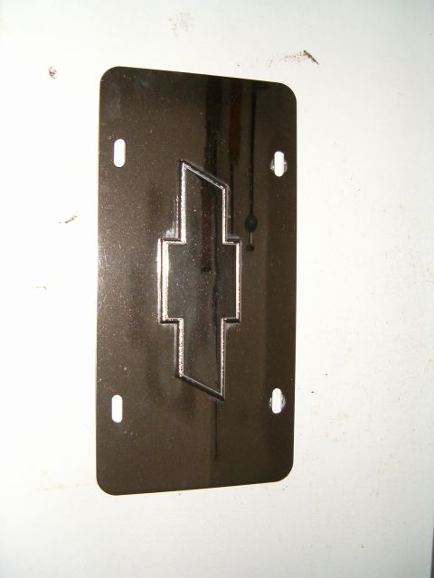1991 Ford Bronco - A chrome Chevrolet emblem is affixed to a dark license plate, which has four mounting holes for attachment.