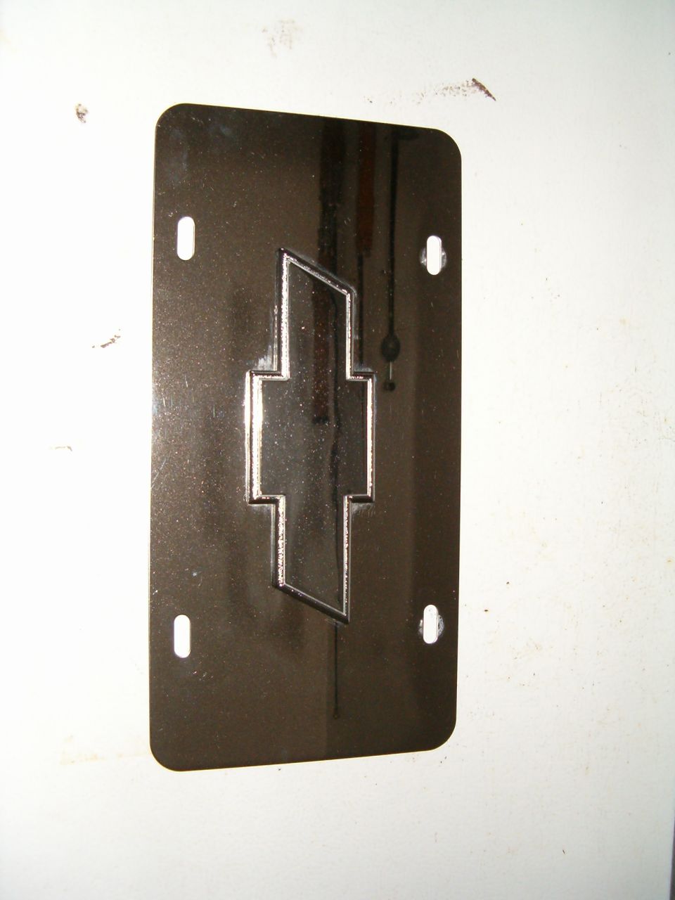 Chrome Chevrolet emblem on a dark license plate with four mounting holes