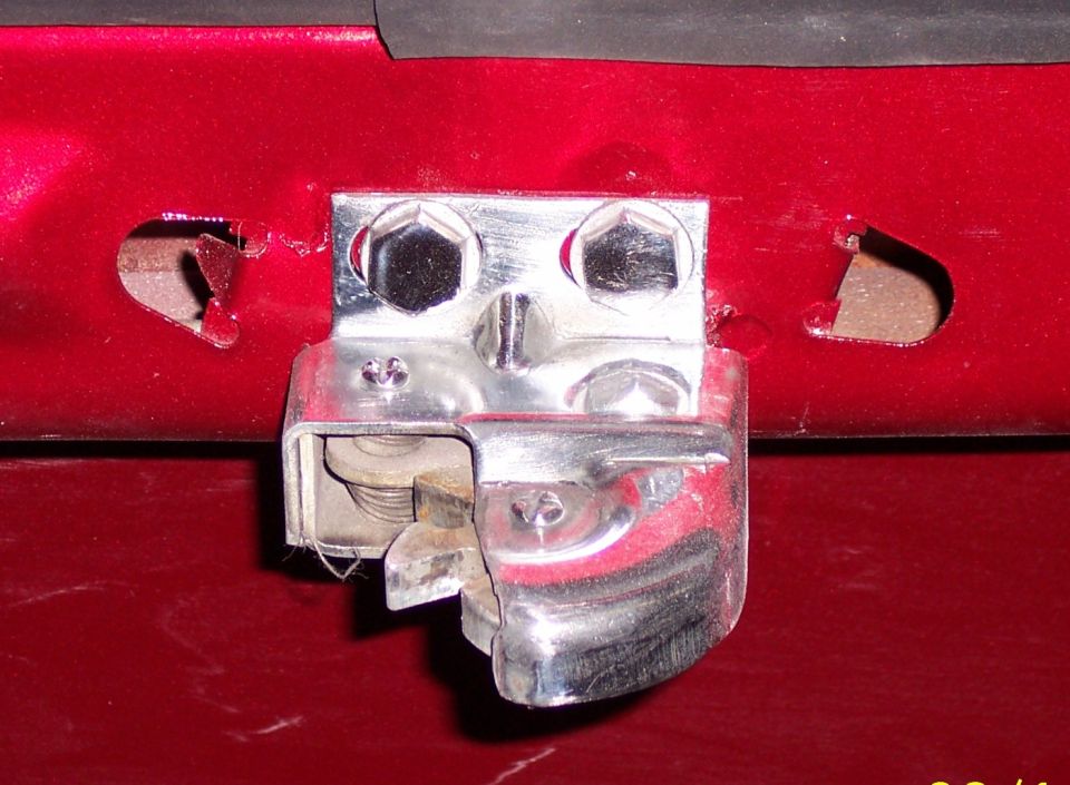 Chrome door latch mechanism bolted to red-painted panel on a 1960 Ford Falcon