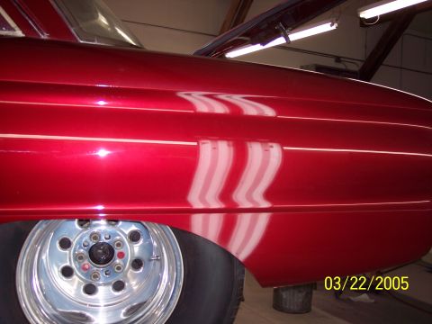 1960 Ford Falcon - A close-up view of a red car's side panel and wheel, showing reflections on the metallic paint.