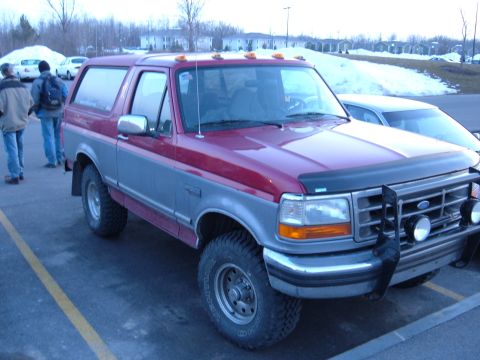 1995 Ford Bronco - Two-tone red over silver full-size Ford Bronco parked in a snowy lot, seen from the passenger-side front three-quarter. Modified with a bru…