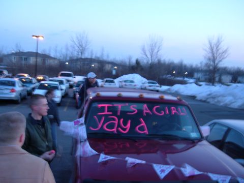 1995 Ford Bronco - Red pickup decorated in a snowy parking lot at dusk, its windshield painted in pink marker reading "IT'S A GIRL! yay a" with pink pennant b…