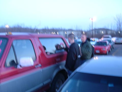 1995 Ford Bronco - Blurry dusk parking-lot shot of a red-over-silver full-size Ford Bronco with an amber roof beacon, its rear side glass being soaped up with…