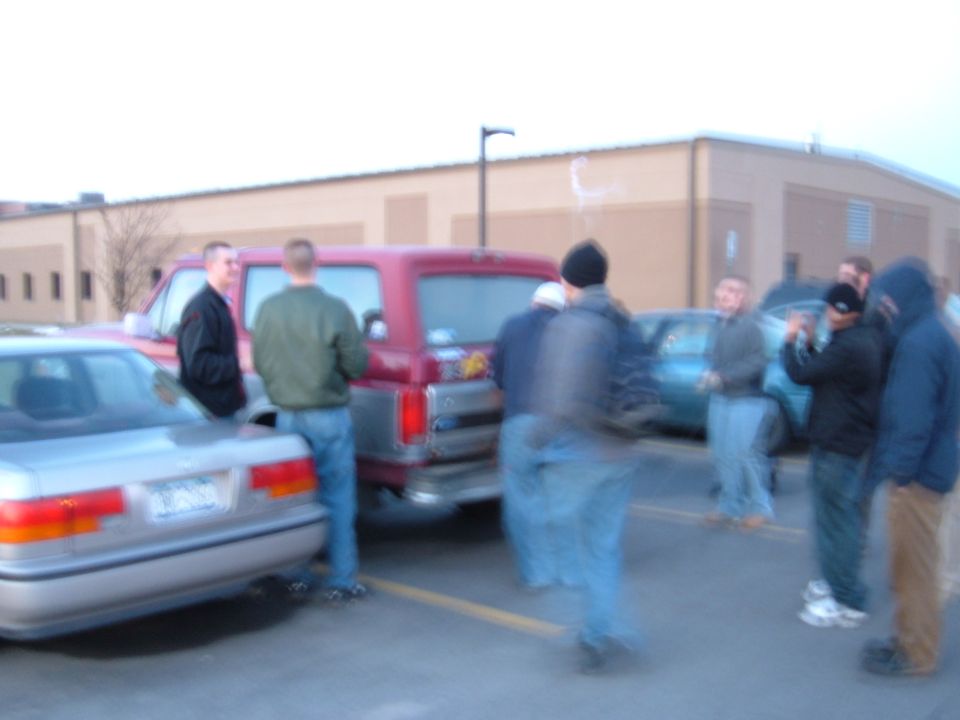 Maroon Ford Bronco parked with people gathered in a parking lot at dusk
