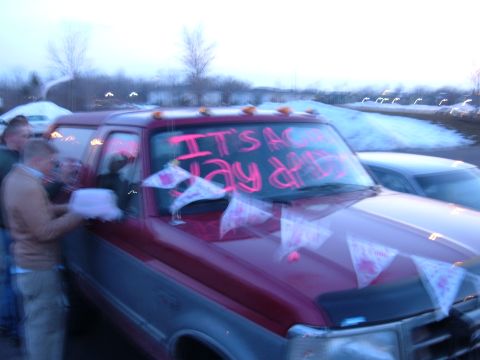 1995 Ford Bronco - Blurry dusk photo of a red-over-gray two-tone Ford Bronco with cab roof marker lights, its windshield painted with "IT'S A GIRL" in pink an…