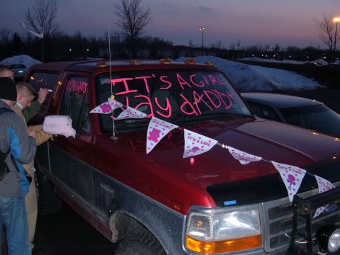 1995 Ford Bronco - Front three-quarter view at dusk of a red full-size Ford Bronco decorated for a baby announcement, with pink "IT'S A GIRL" pennant banners…