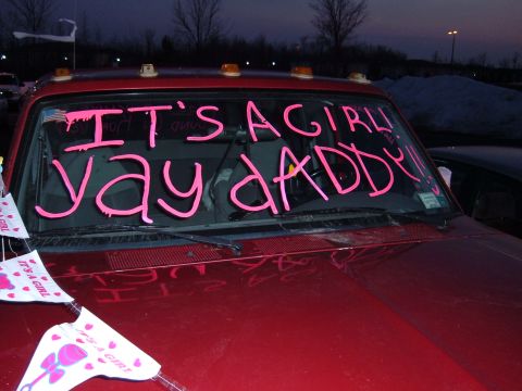 1995 Ford Bronco - Front view of a dark red/maroon vehicle with amber roof marker lights, its windshield painted in pink lettering reading "IT'S A GIRL! YAY D…