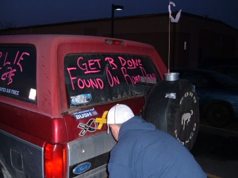 1995 Ford Bronco - Night shot of the rear of a maroon full-size Ford Bronco with "GET R DONE / FOUND ON ROAD DEAD" written in pink on the dusty tailgate glass…