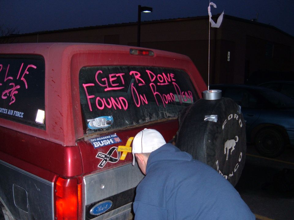 Maroon Ford Bronco tailgate at night with pink window writing and Ford Bronco spare tire cover