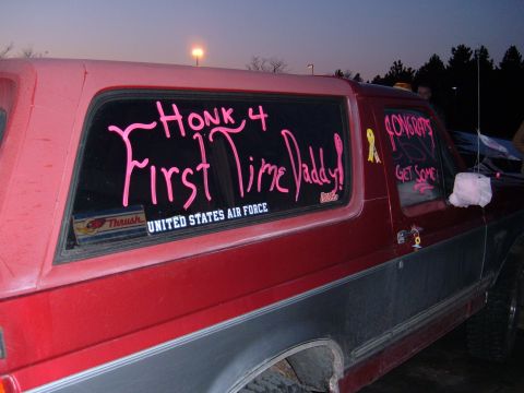 1995 Ford Bronco - Side view of a two-tone red-over-gray Ford Bronco SUV at dusk, with pink window paint reading 'HONK 4 First Time Daddy!' and 'CONGRATS GET…